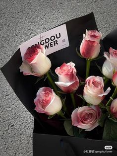 a bunch of pink and white roses are in a black box with a tag on it