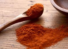 a wooden spoon filled with red powder next to a bowl full of ground cinnamons