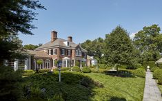 a large brick house sitting on top of a lush green field next to a forest