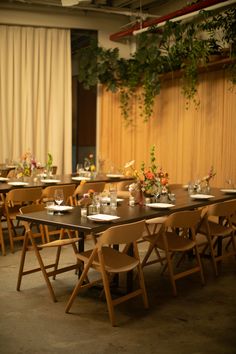 the tables are set up for an event with flowers and greenery hanging from the ceiling