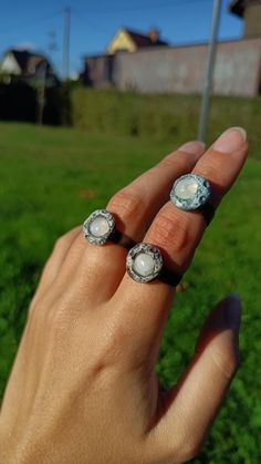 a woman's hand with two rings on her fingers in front of a green field