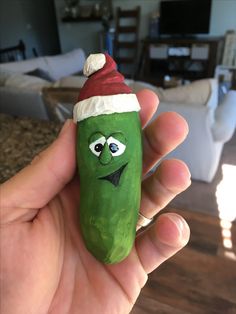 a hand holding a green pepper with a santa hat on it's head and eyes