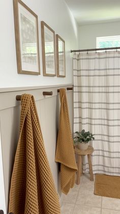 two towels hanging on the wall in front of a shower curtain and some stools