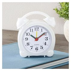 a white alarm clock sitting on top of a table next to a potted plant