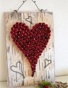 a heart made out of red beads hanging on a white wall next to a plant