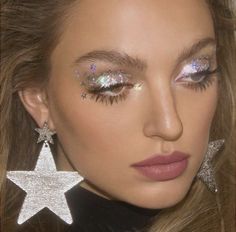 a close up of a woman with glitter on her face and star shaped earring