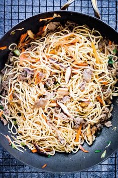 a wok filled with noodles and meat on top of a table