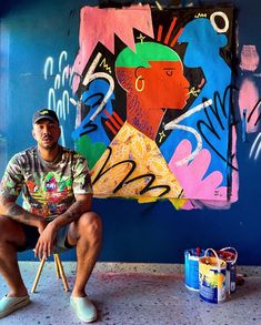 a man sitting on a chair in front of a wall with colorful paintings and paintbrushes