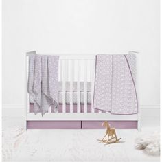 a white crib with purple bedding and a toy horse on the floor next to it