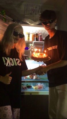 two people standing next to each other in front of an open refrigerator with food on it