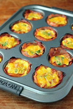 an open muffin tin filled with eggs and ham on a wooden table, ready to be eaten