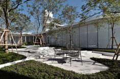 an outdoor play area with swings, chairs and tables in front of a white building