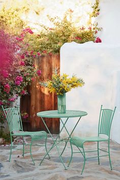 an outdoor table and chairs with flowers in the background