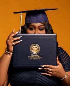 a woman wearing a graduation cap and gown holding up a black book with gold lettering on it