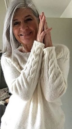 an older woman is smiling and holding her hand up to her face while wearing a white sweater