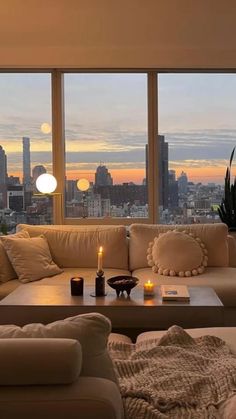 a living room filled with furniture and a large window overlooking the cityscape at sunset