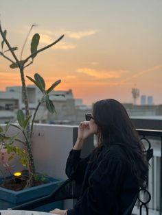 a woman sitting at a table on top of a balcony next to a potted plant