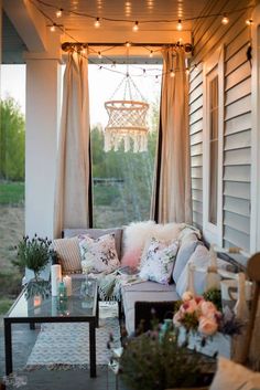 an outdoor living room with lights strung from the ceiling and curtains on the windowsill