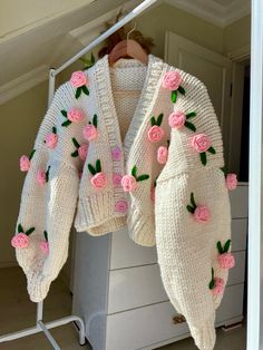 a white sweater with pink roses on it hanging from a clothes rack in a closet