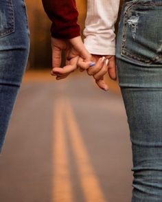 two people holding hands while standing next to each other on a street with their fingers together