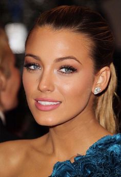 a close up of a woman wearing a blue dress and earrings with her hair in a pony tail