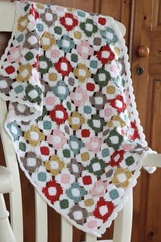 a crocheted blanket sitting on top of a white chair next to a wooden door