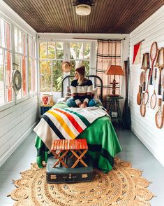 a woman sitting on top of a bed in a room with lots of windows and rugs