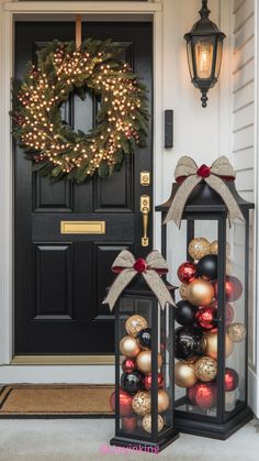 two lanterns with christmas ornaments on them sitting in front of a door decorated for the holidays