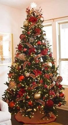 a decorated christmas tree with red and gold ornaments in a living room area, next to a window