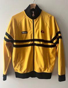 This Ellesse vintage black and yellow jacket is one of a kind!! It has long sleeves, joyful bright colors, stylish zipper, very good condition! Details: - Size on tag S (Small). Jacket fits easy on size M person (for more info please look in Measurements),    - 2 side pockets, - Closure: very nice zipper, - condition- excellent, although please note small stains on the right pocket (you can see them in photo). Measurements*: - Length: 68 cm, - Bust width: 53 cm (armpit to armpit), - Bottom edge Retro Long Sleeve Track Jacket For Winter, Casual Yellow Long Sleeve Outerwear, Yellow Long Sleeve Track Jacket For Winter, Yellow Hooded Track Jacket For Winter, Casual Yellow Track Jacket For Fall, Casual Yellow Long Sleeve Track Jacket, Vintage Mustard Long Sleeve Outerwear, Sporty Yellow Long Sleeve Outerwear, Black And Yellow Jacket