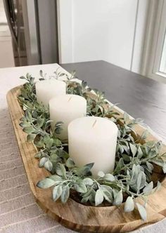 three candles sitting on top of a wooden tray filled with greenery