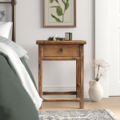 a small wooden table sitting next to a bed in a room with a painting on the wall