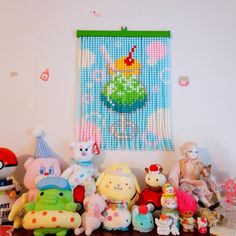 there are many stuffed animals on the table together in front of a wall hanging with pictures