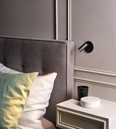 a nightstand with a cup on it next to a gray headboard and white pillows