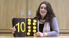 a woman sitting at a table holding up a book with yellow buttons on the cover