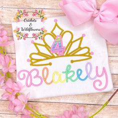 a pink bow and some flowers on a wooden table with a white t - shirt that says, buckleley