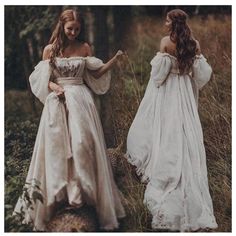 two women in white dresses standing next to each other on the grass with trees in the background