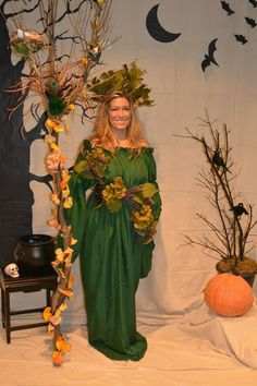 a woman in green dress standing next to a tree with leaves and flowers on it