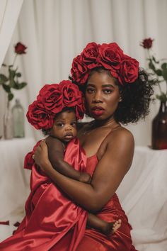 a woman in a red dress holding a small child with flowers on her head and arms