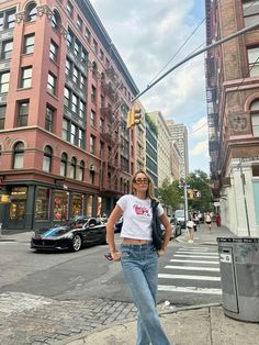 a woman standing on the side of a road next to tall buildings