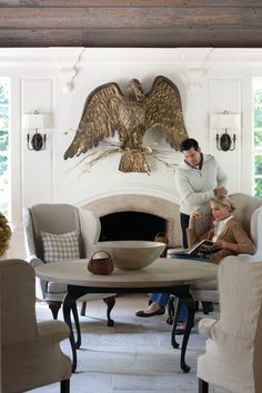 a man and woman standing in front of a fireplace with an eagle on the mantle