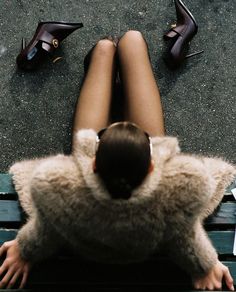 a woman sitting on top of a wooden bench next to high heel shoes and papers