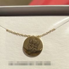 a gold plated necklace with a cat on it's face in a box