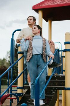 a man and woman standing next to each other in front of a playground structure with stairs