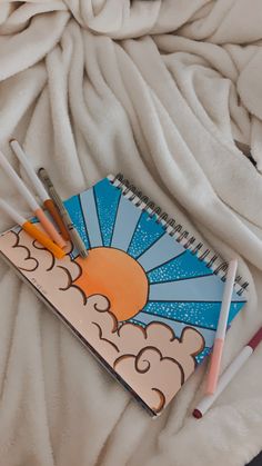 an open notebook with three pencils on top of it and the sun in the background