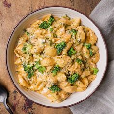 a white bowl filled with pasta and broccoli on top of a wooden table