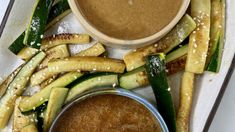 an arrangement of vegetables and dipping sauce on a tray with a white surface, including zucchini