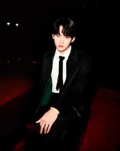 a young man in a suit and tie sitting on a red chair at night time