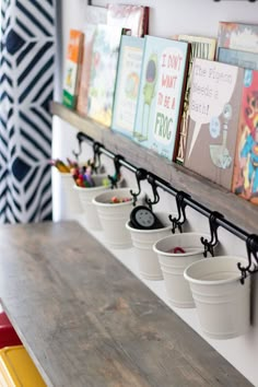 several buckets are lined up on the wall next to a shelf with children's books