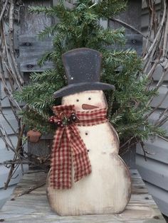 a wooden snowman sitting on top of a table next to a potted plant